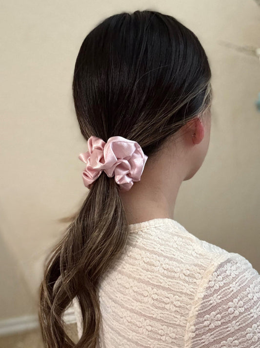 Person with long dark hair tied in a ponytail with a pink scrunchie, wearing a white textured top.