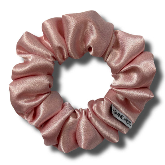 Pink satin scrunchie with a brand label on a white background