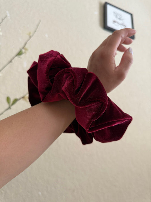 Maroon scrunchie on a wrist with a neutral background