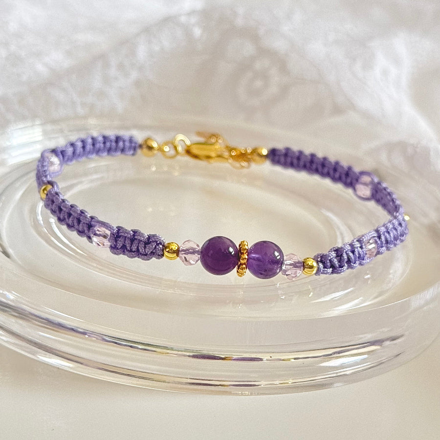 Purple beaded bracelet with gold accents on a clear glass surface