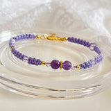 Purple beaded bracelet with gold accents on a clear glass surface
