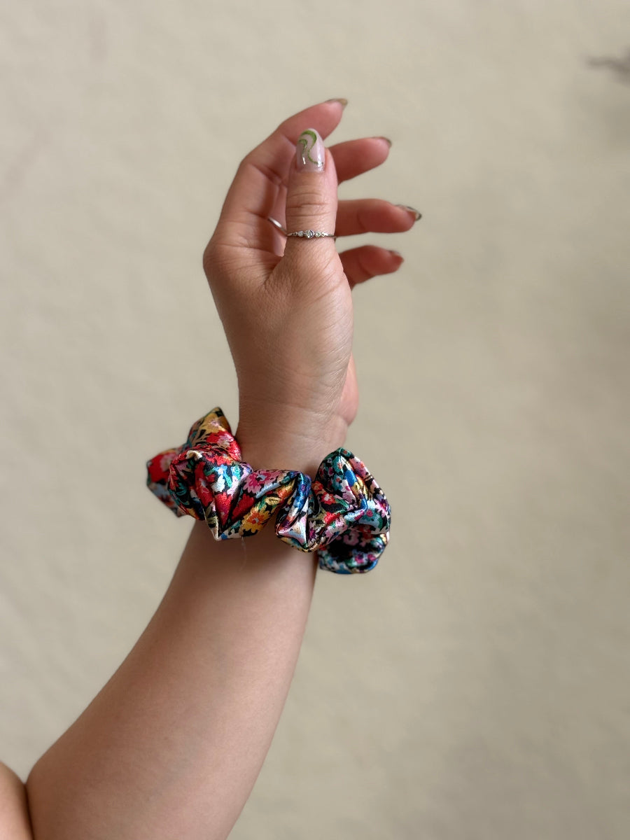 Hand wearing a colorful scrunchie on a plain background