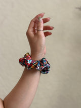 Hand wearing a colorful scrunchie on a plain background