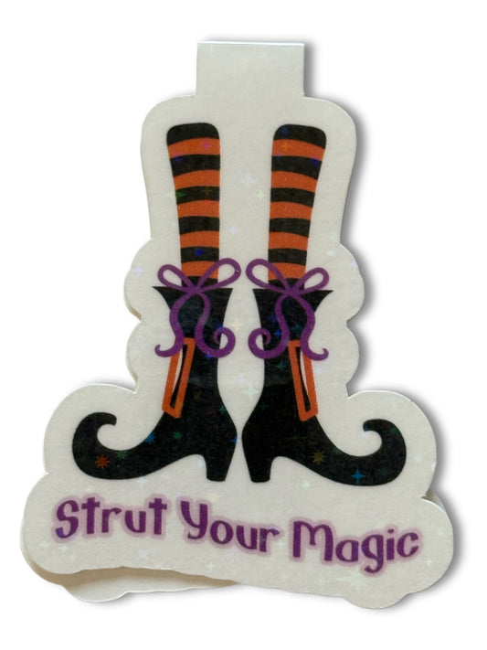 Decorative sign with witch legs and 'Strut Your Magic' text on a white background